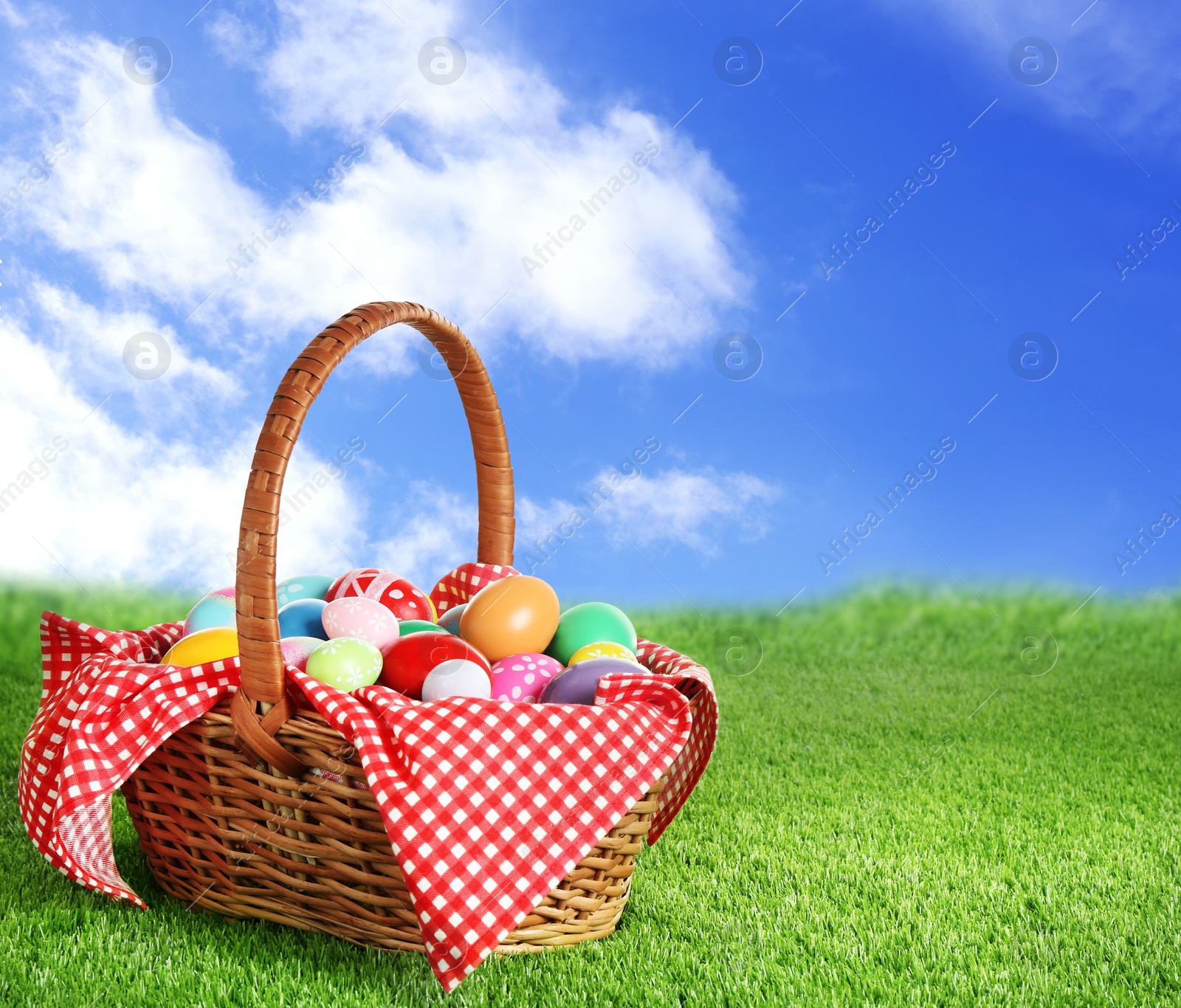 Image of Wicker basket with Easter eggs on green grass outdoors, space for text