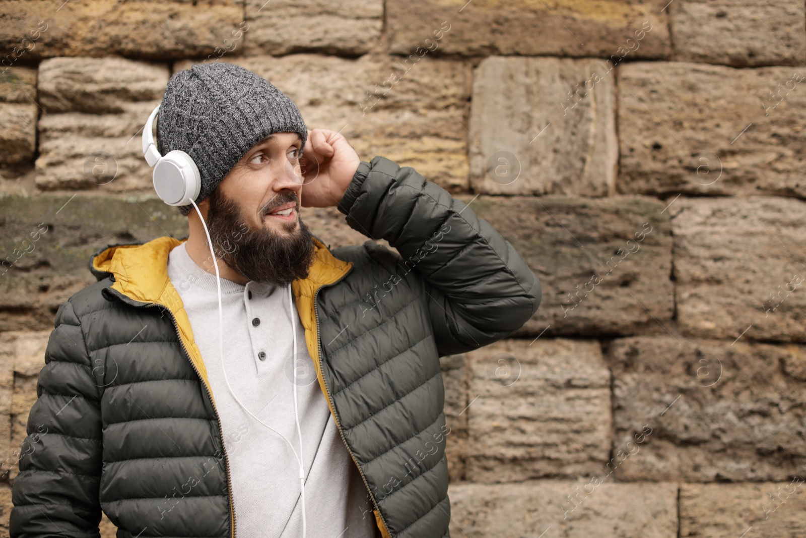 Photo of Mature man with headphones listening to music near stone wall. Space for text