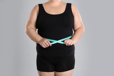 Photo of Overweight woman measuring waist before weight loss on color background