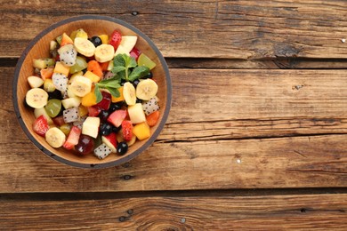 Photo of Delicious exotic fruit salad on wooden table, top view. Space for text