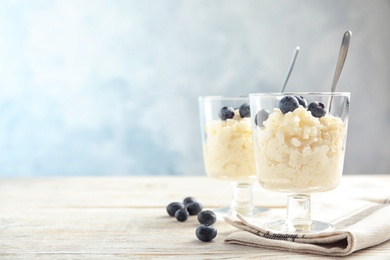 Photo of Creamy rice pudding with blueberries in dessert bowls on table. Space for text