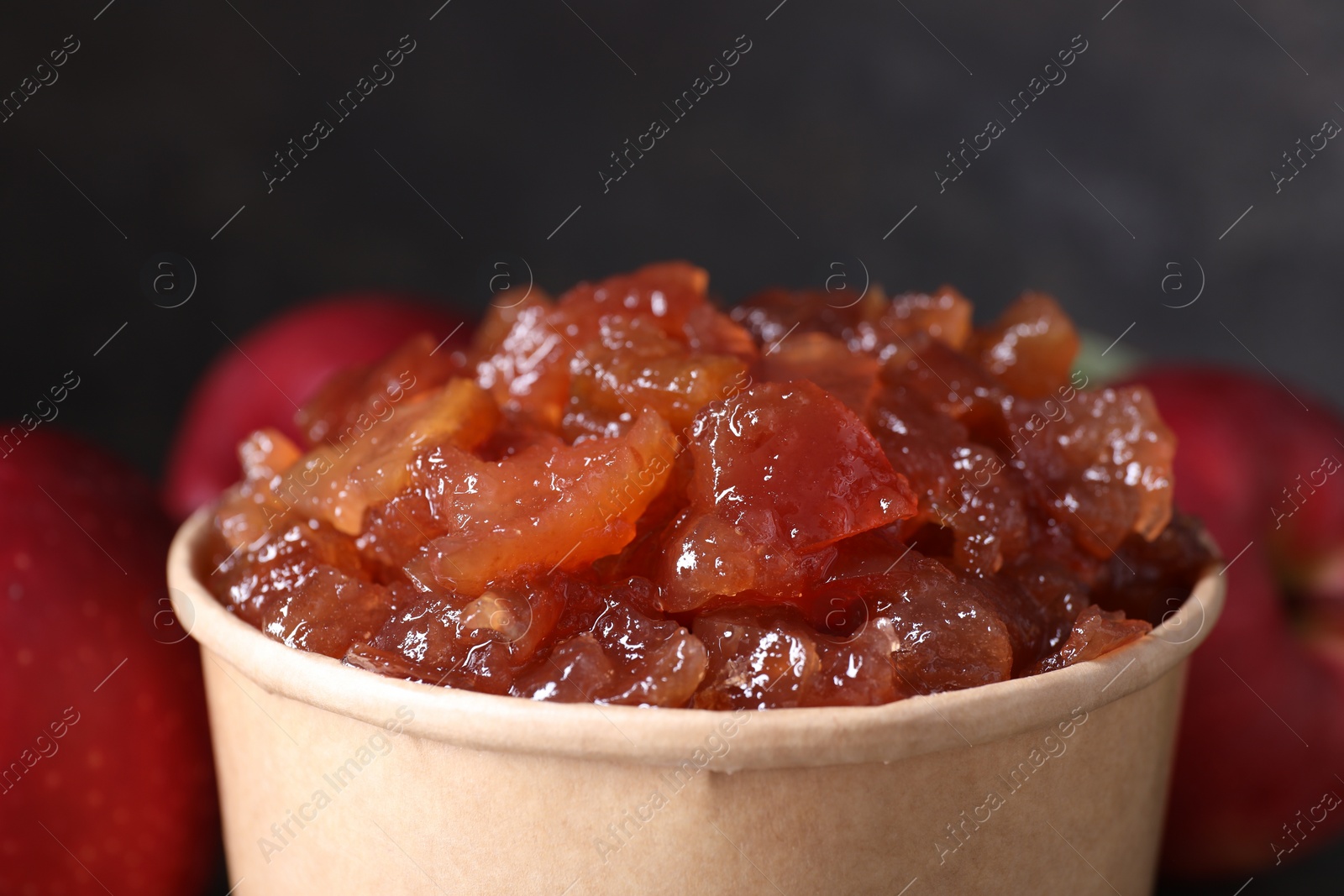 Photo of Delicious apple jam in paper cup and fresh fruits, closeup