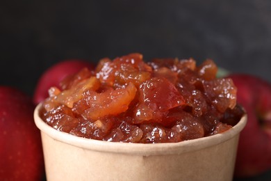 Photo of Delicious apple jam in paper cup and fresh fruits, closeup