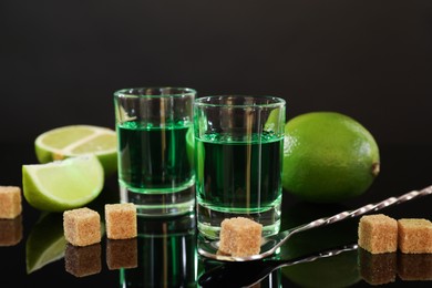 Photo of Absinthe in shot glasses, brown sugar, lime and spoon on mirror table. Alcoholic drink
