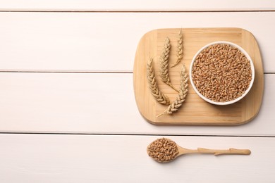 Wheat grains with spikelets on white wooden table, flat lay. Space for text