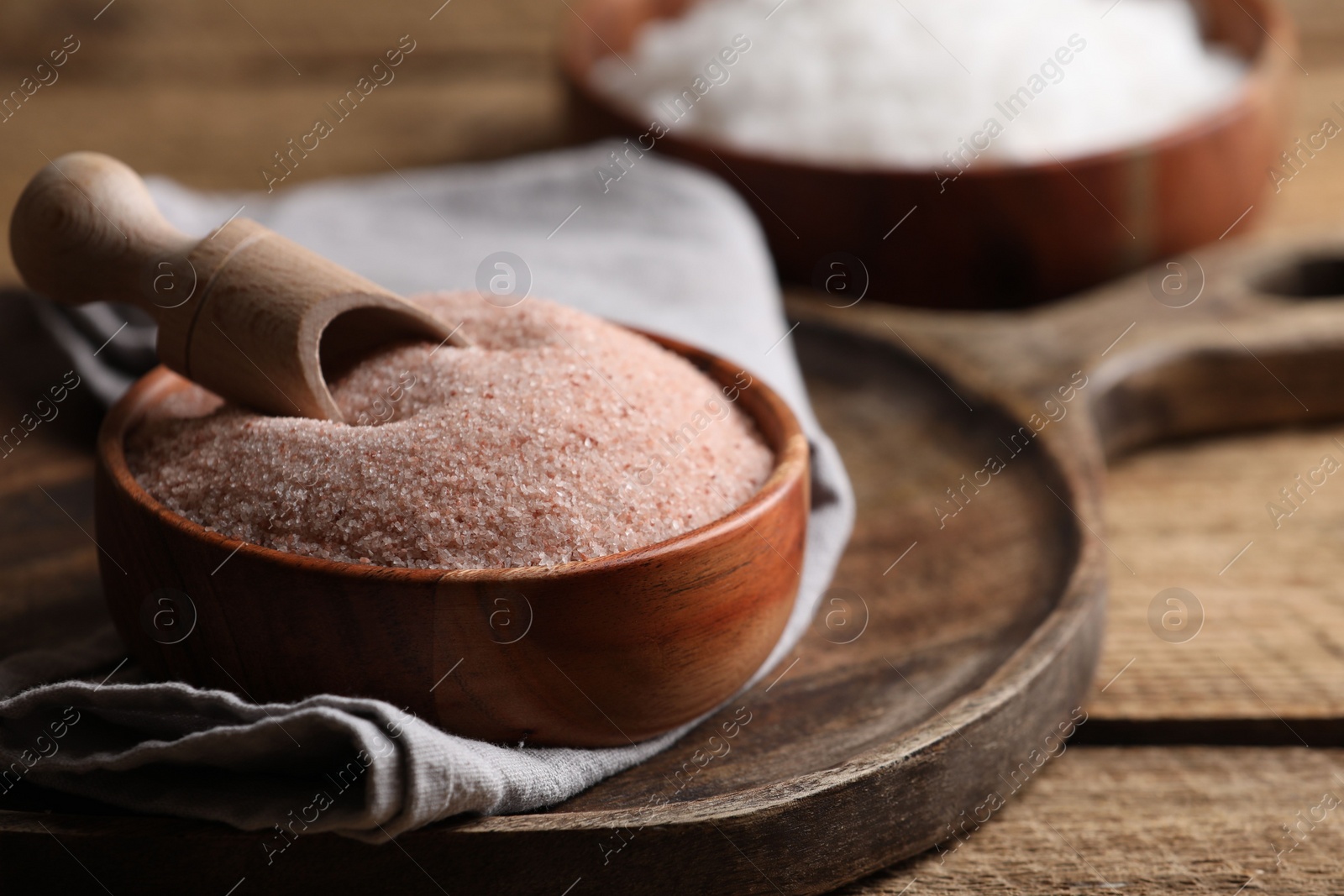 Photo of Different salt and scoop in bowl on wooden table, closeup. Space for text