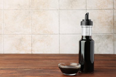 Bottle and bowl with soy sauce on wooden table. Space for text