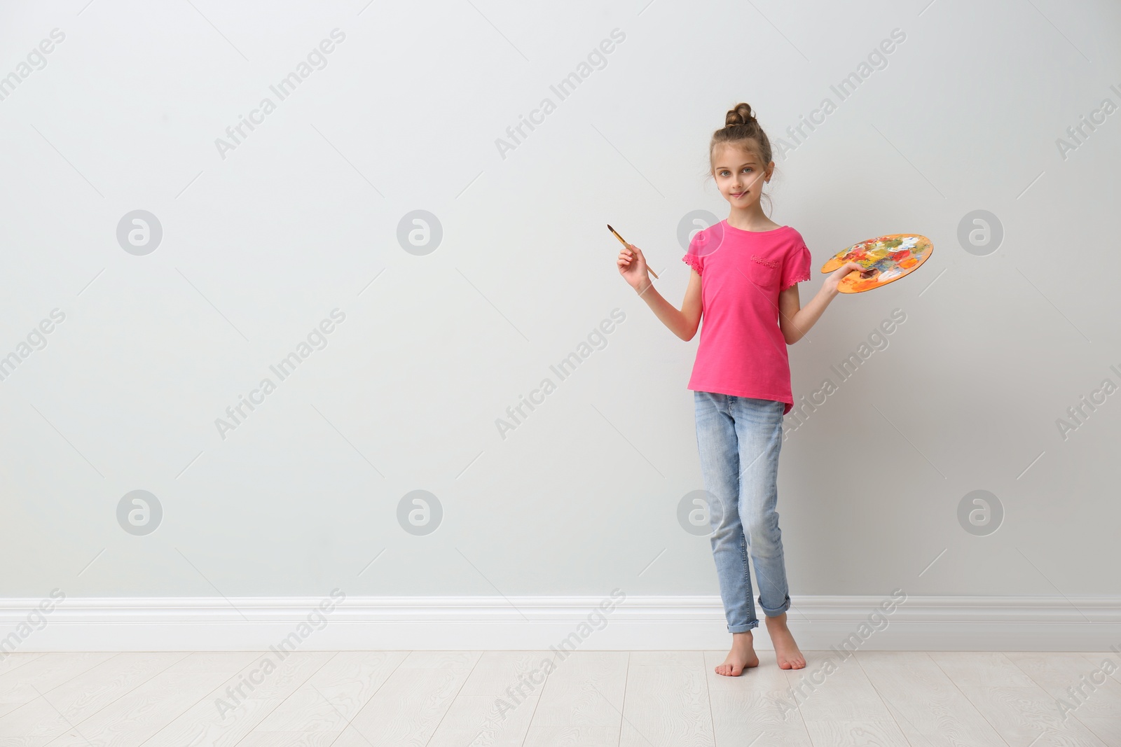 Photo of Little girl with brush and paint palette near light wall indoors. Space for text