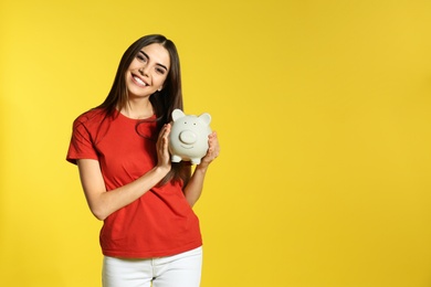 Young woman with piggy bank on color background, space for text. Money saving