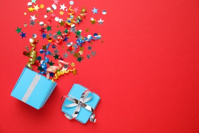 Box with bright confetti on red background, flat lay. Space for text