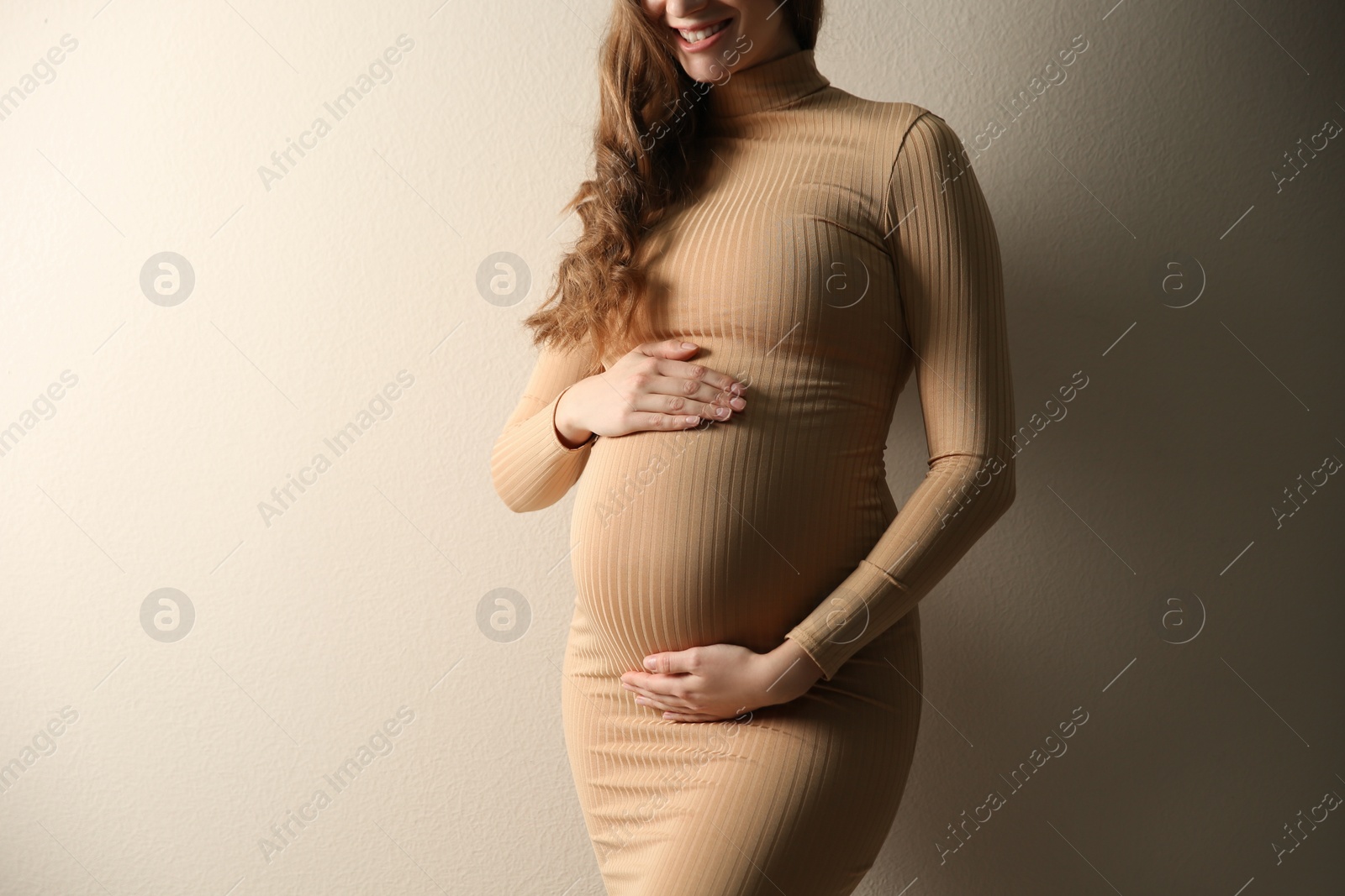 Photo of Pregnant woman touching her belly on beige background, closeup