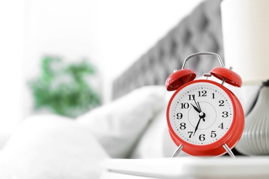 Photo of Analog alarm clock on table in bedroom. Time of day