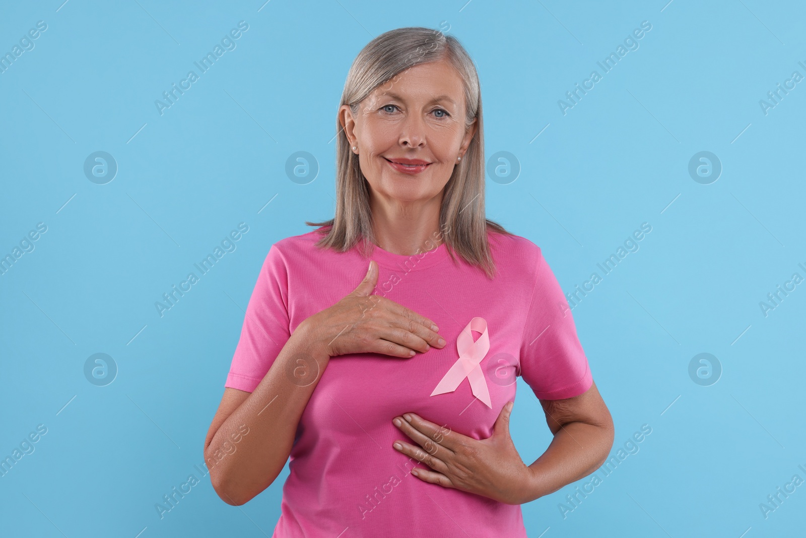 Photo of Senior woman with pink ribbon on light blue background. Breast cancer awareness