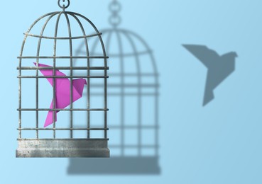 Image of Freedom. Caged origami bird and it's released shadow on light blue background