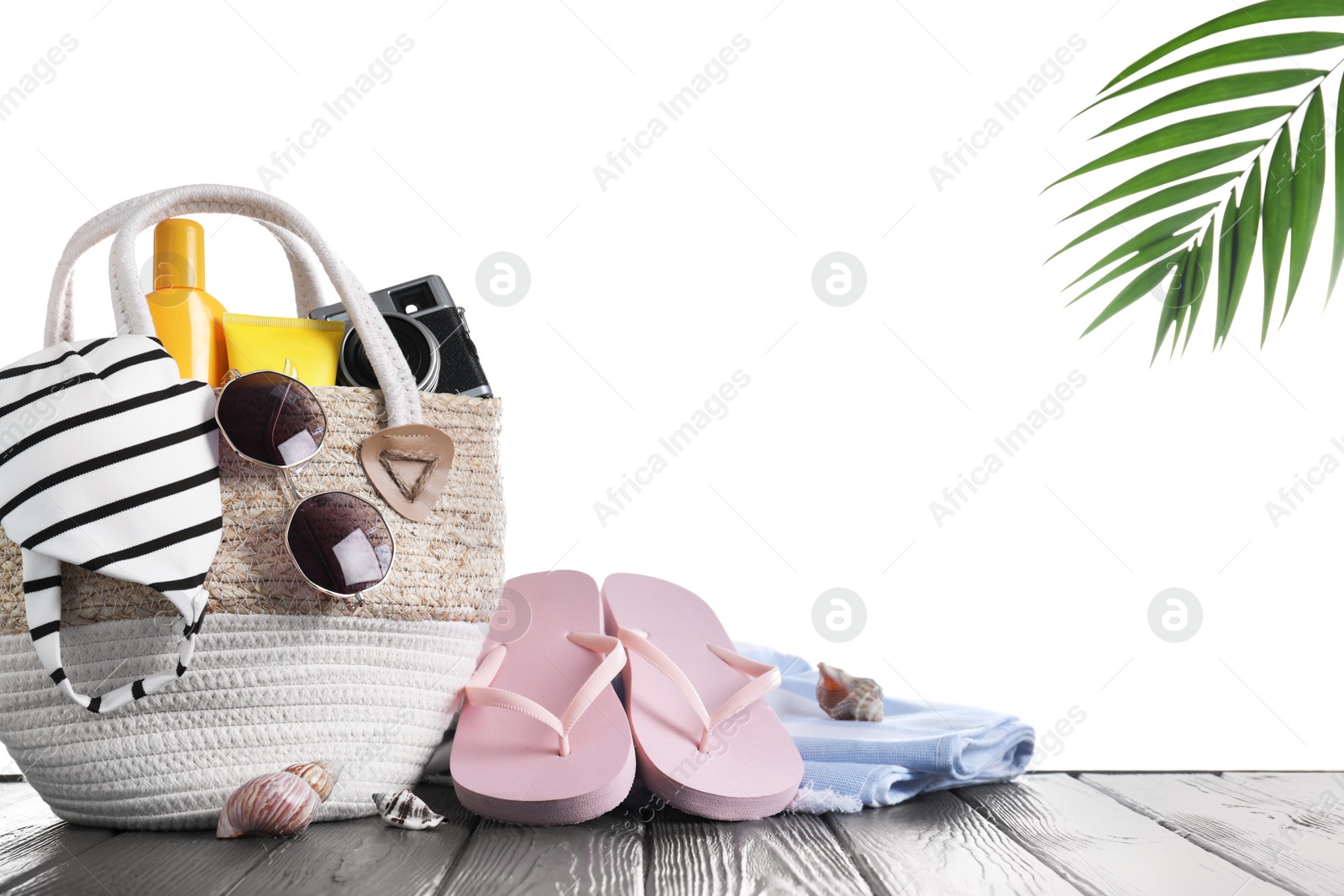 Photo of Bag with different beach objects on grey wooden table against white background