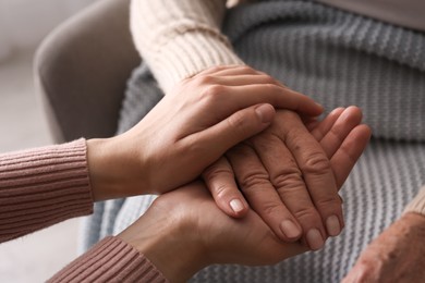 Photo of Young and elderly women holding hands together on blurred background, closeup