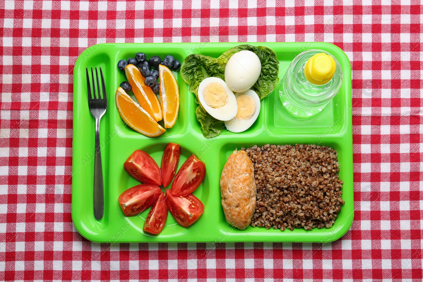 Photo of Serving tray with healthy food on checkered background, top view. School lunch