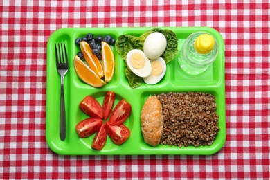 Serving tray with healthy food on checkered background, top view. School lunch