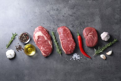 Photo of Raw beef steaks, oil and spices on grey table, flat lay