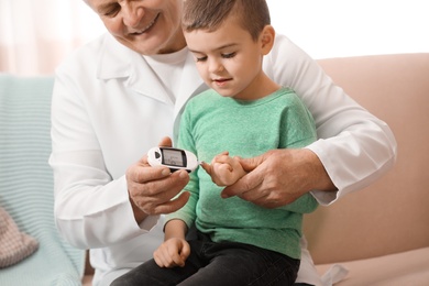 Doctor measuring patient's blood sugar level with digital glucose meter at home. Diabetes control