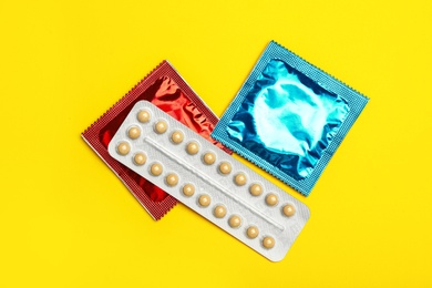 Condoms and birth control pills on yellow background, flat lay. Safe sex concept