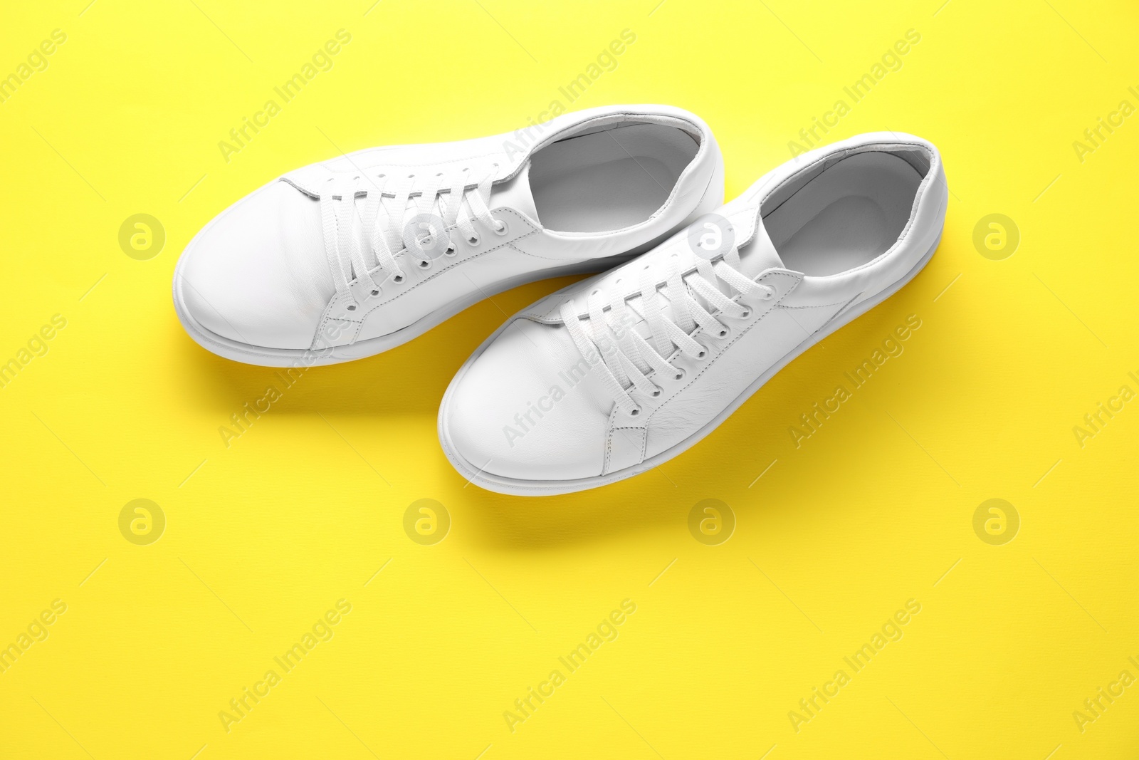 Photo of Pair of stylish white sneakers on yellow background, top view