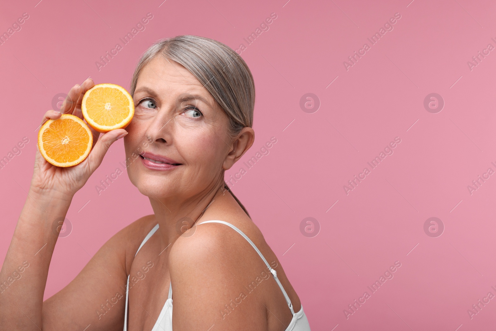 Photo of Beautiful woman with halves of orange rich in vitamin C on pink background, space for text