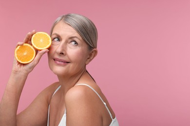 Photo of Beautiful woman with halves of orange rich in vitamin C on pink background, space for text