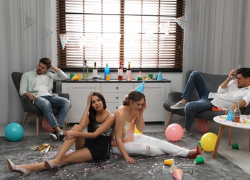 Photo of Group of friends suffering from hangover in messy room after party