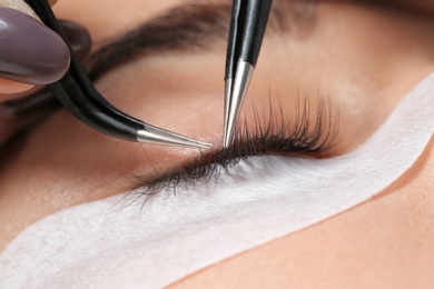 Young woman undergoing eyelashes extensions procedure, closeup