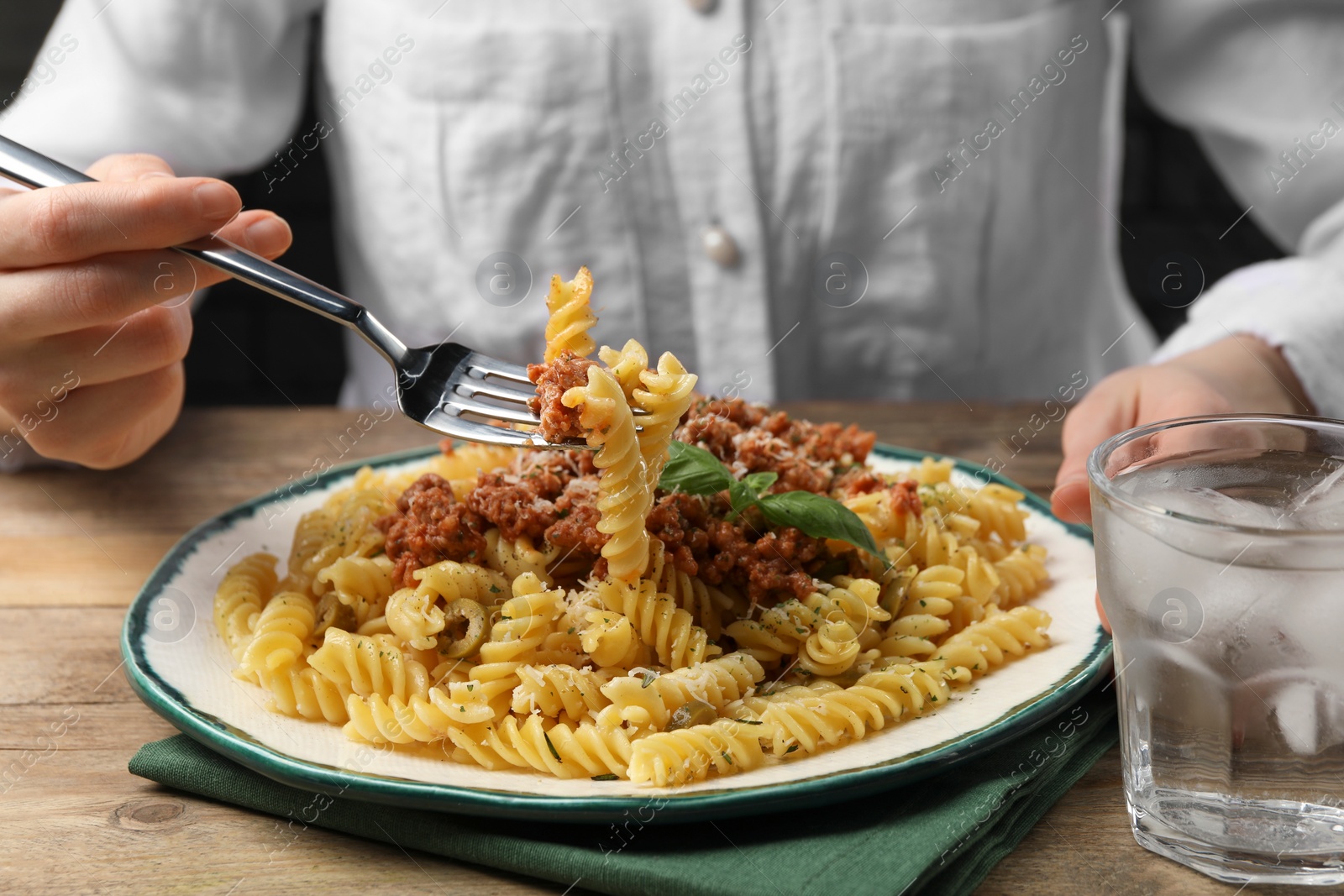 Photo of Woman eating delicious pasta with minced meat and basil at wooden table, closeup