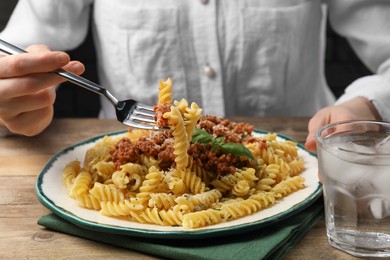 Photo of Woman eating delicious pasta with minced meat and basil at wooden table, closeup