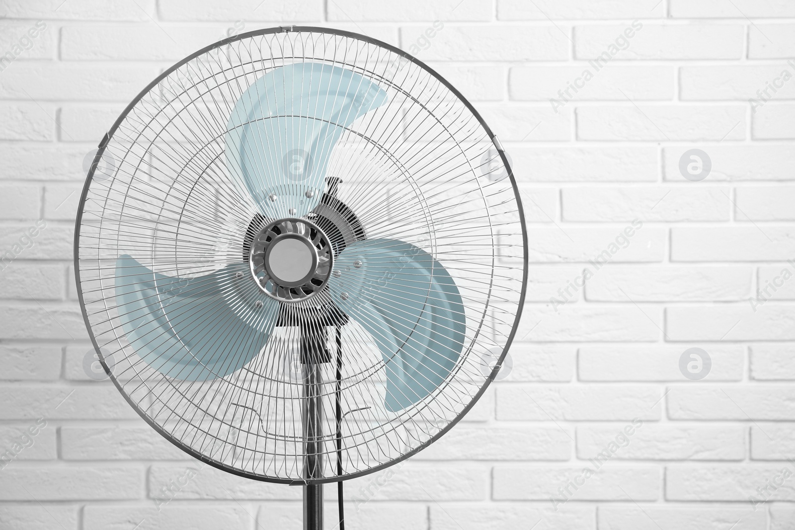Photo of Electric fan near white brick wall. Summer heat