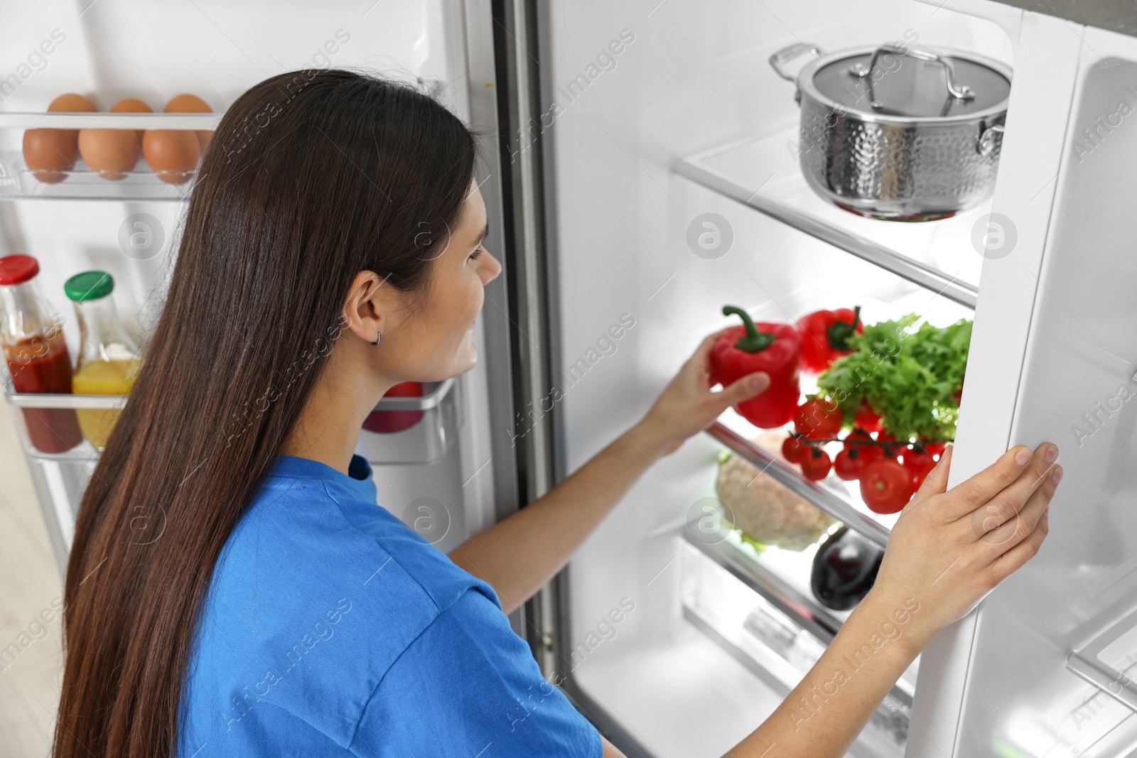 Photo of Young woman taking red bell pepper out of refrigerator