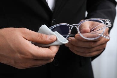 Photo of Man wiping glasses with microfiber cloth on light background, closeup