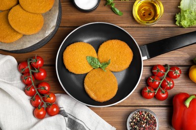 Photo of Delicious fried breaded cutlets, spices and vegetables on wooden table, flat lay