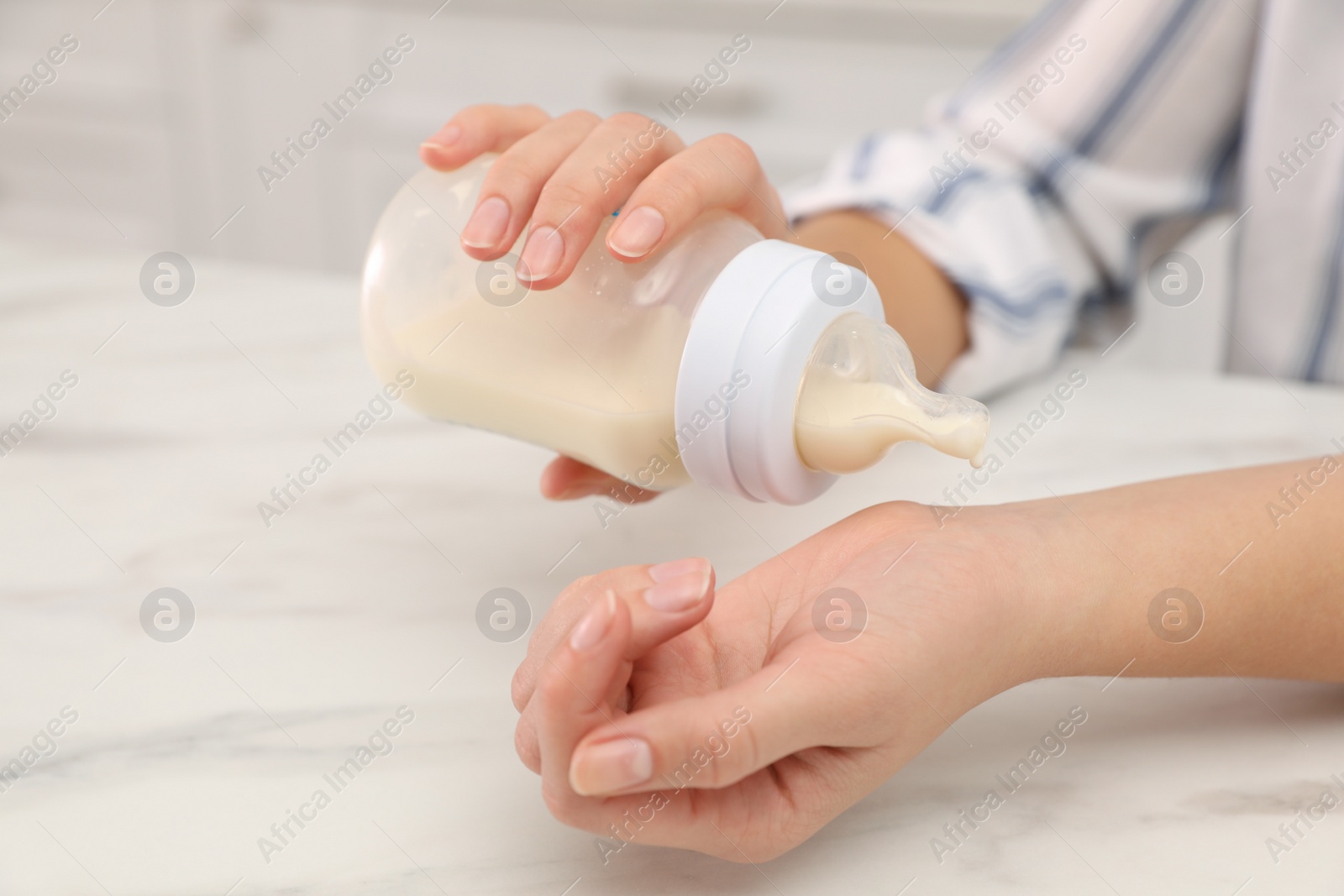 Photo of Woman checking temperature of infant formula at table, closeup. Baby milk