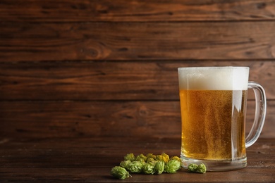 Composition with tasty beer and fresh green hops on wooden background. Space for text