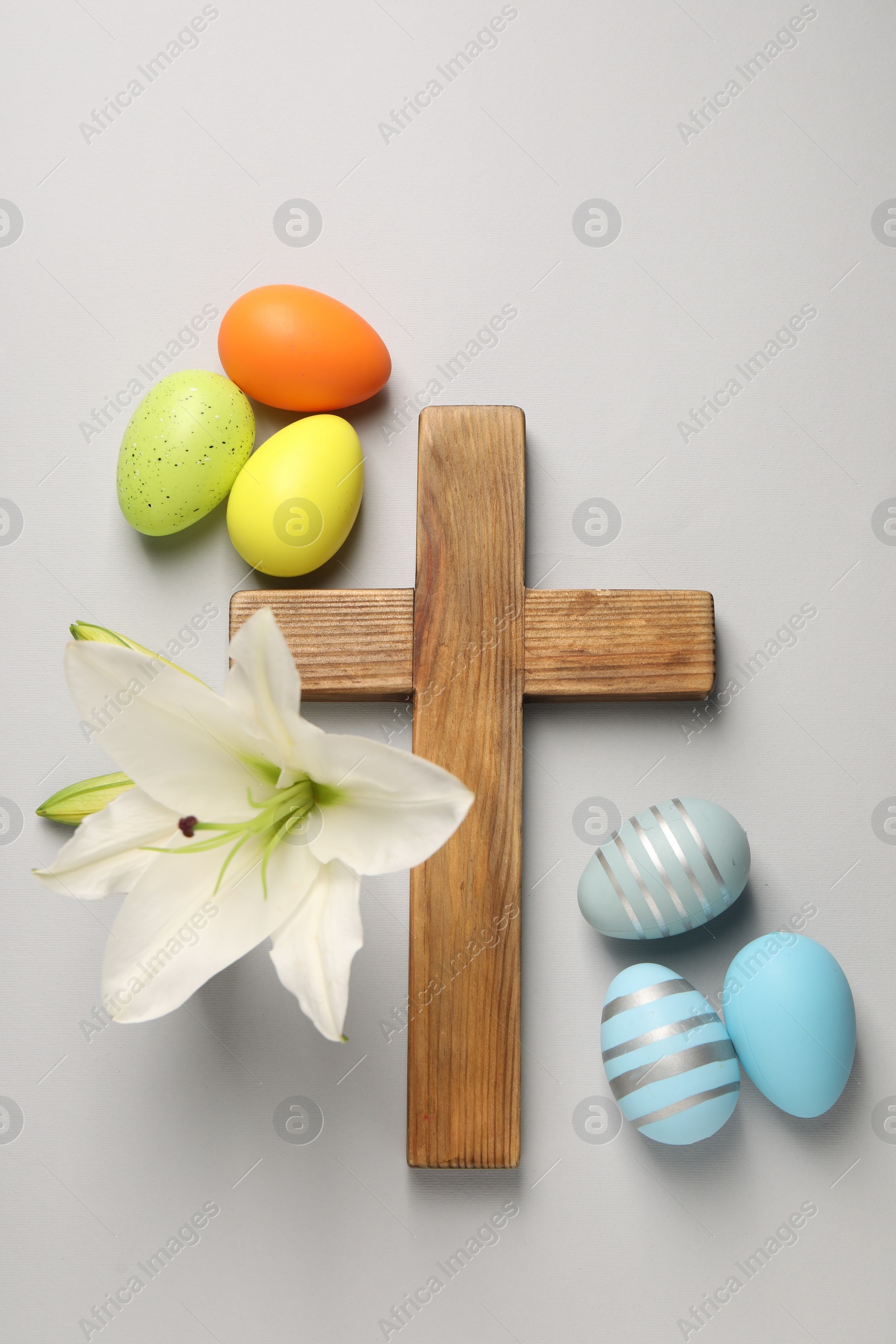 Photo of Wooden cross, painted Easter eggs and lily flowers on grey background, flat lay