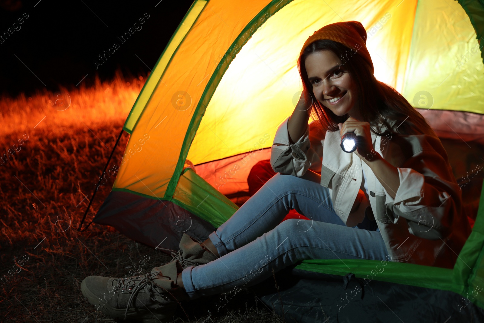 Photo of Young woman with flashlight sitting in tent at night