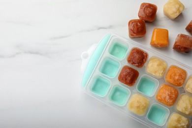 Photo of Different fruit puree in ice cube tray on white marble table, flat lay. Space for text