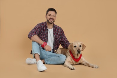 Photo of Happy man with his cute Labrador Retriever on beige background
