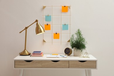 Photo of Memo board with colorful notes hanging on white wall over desk indoors