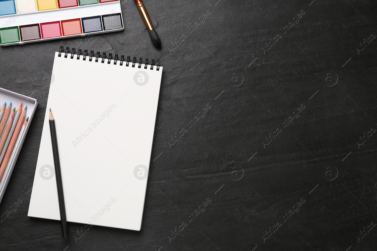 Photo of Flat lay composition with blank sketchbook on black slate table. Space for text