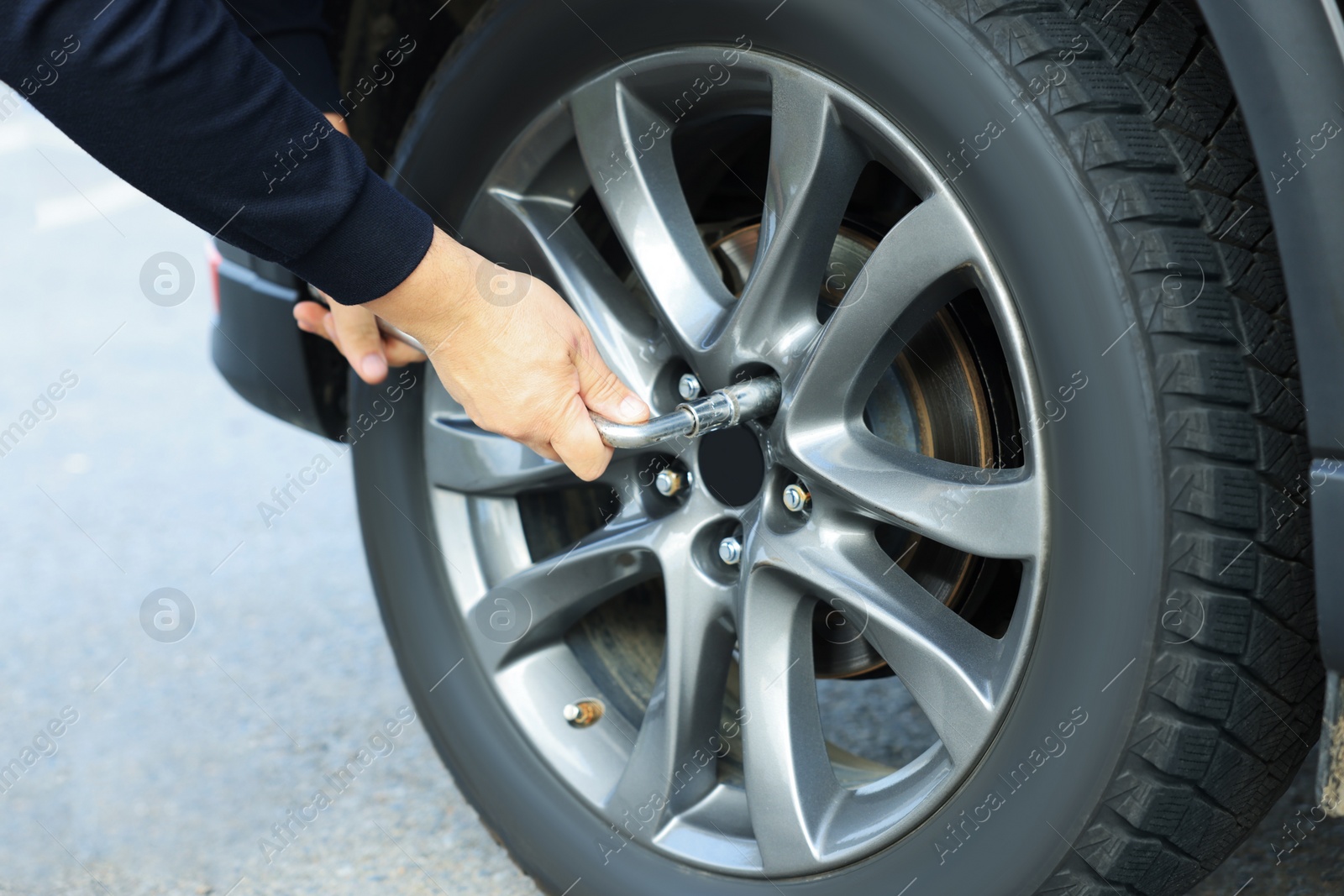 Photo of Man changing tire of car outdoors, closeup