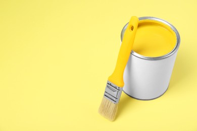 Photo of Can of paint and brush on pale yellow background. Space for text