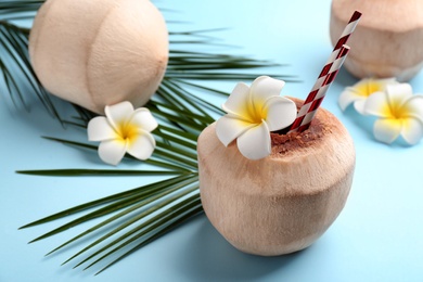 Photo of Fresh coconut with drinking straws and flowers on light blue background