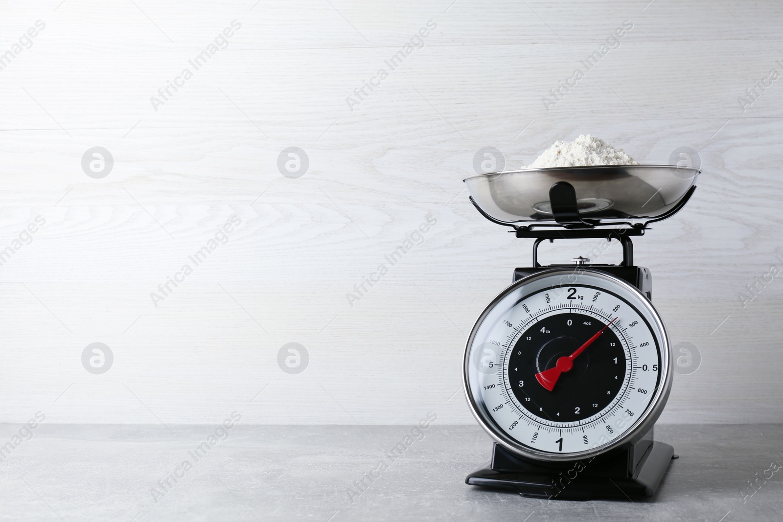 Photo of Kitchen scale with flour on grey table. Space for text