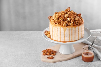 Caramel drip cake decorated with popcorn and pretzels on light table, space for text