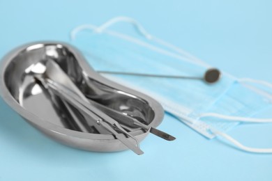 Photo of Kidney shaped tray with set of dentist's tools on light blue background, closeup. Space for text